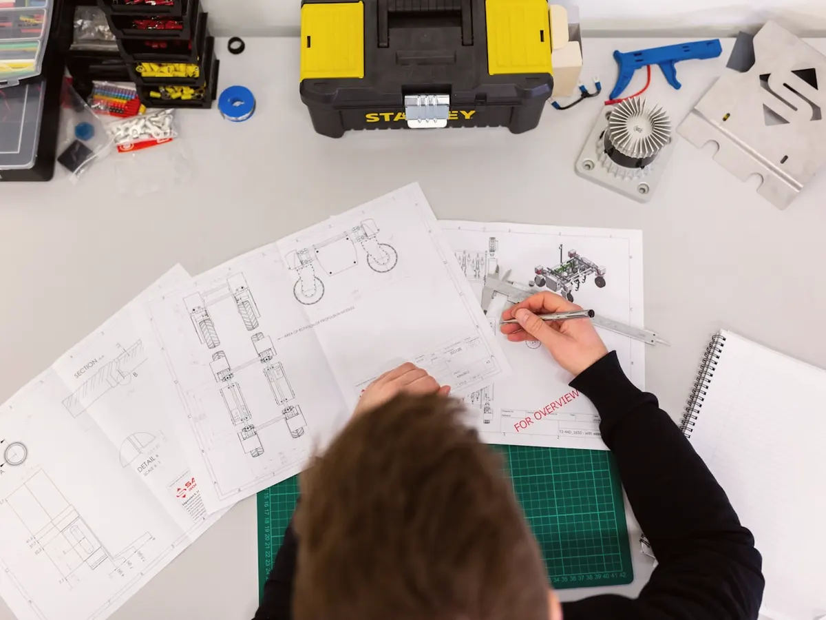 A person sketching a design on paper at a workbench, seen from above